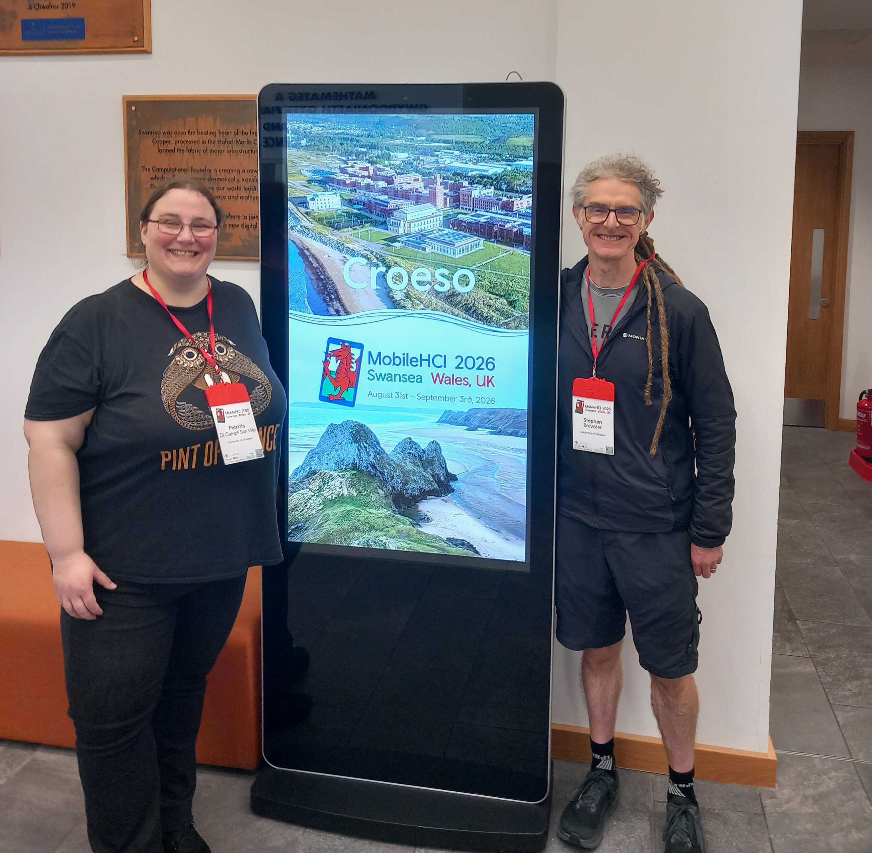 Stephen and Patrizia standing next to a digital banner of the MobileHCI conference